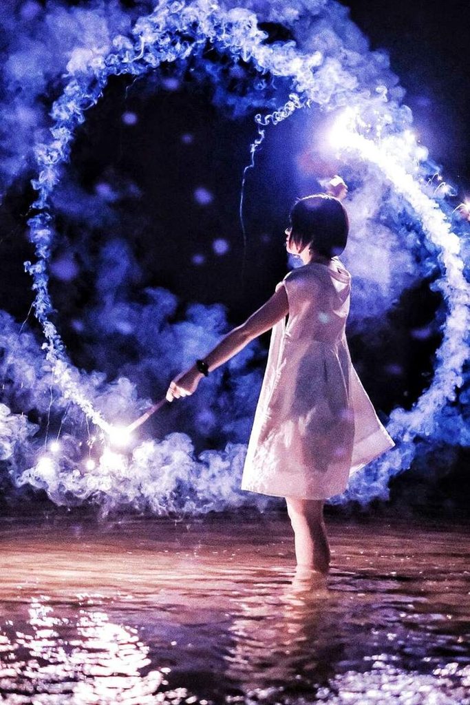 Jeune femme en robe blanche debout dans une eau bleutée sous une lumière violette.
