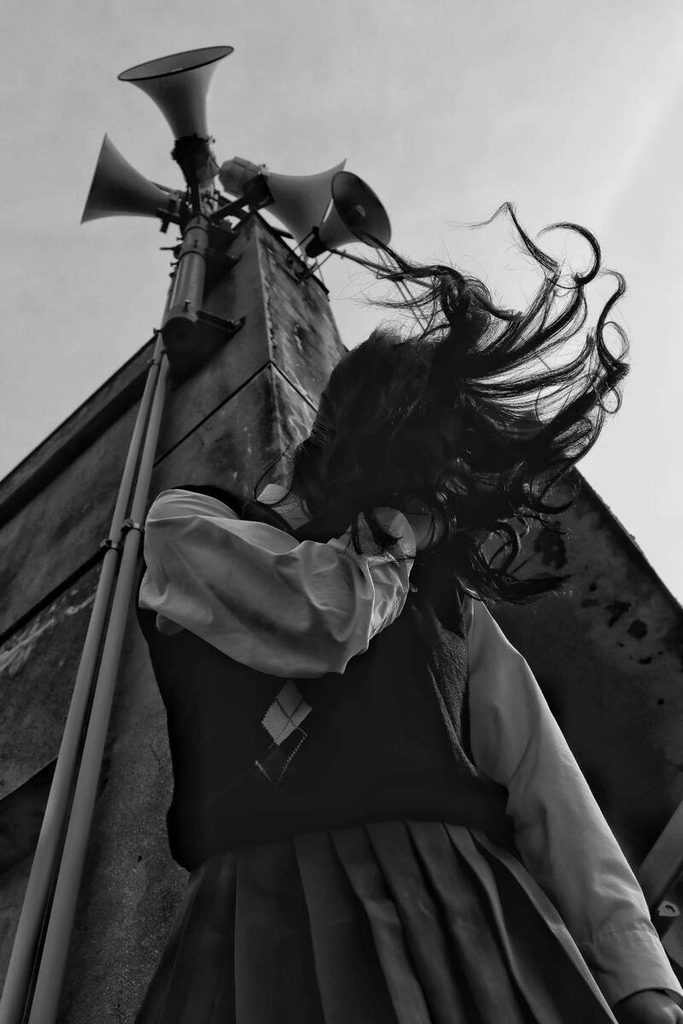 Jeune femme aux cheveux emportés par le vent, photographiée en noir et blanc près de haut-parleurs.
