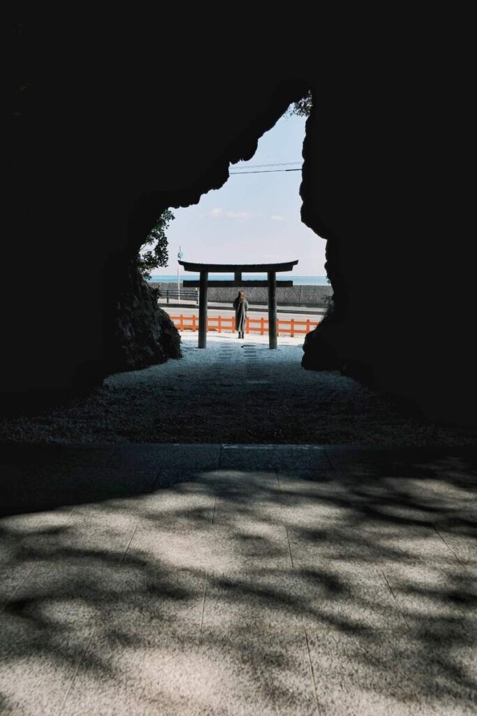 Porte torii japonaise et paysage marin vus à travers l’ouverture sombre d’une grotte.