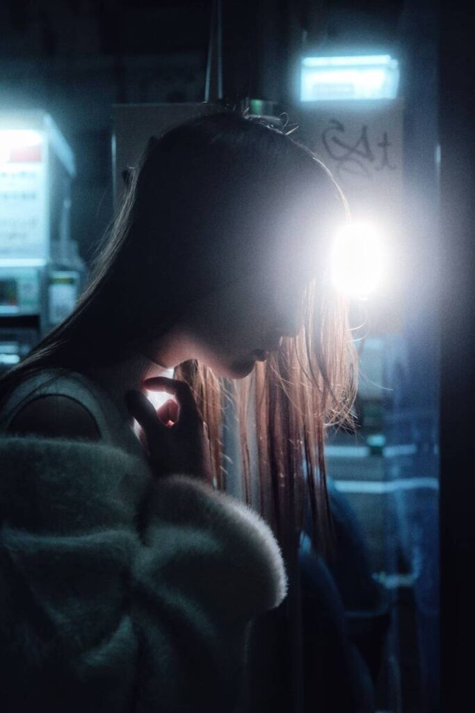 Femme de profil dans une rue sombre, éclairée par une lumière bleue et blanche.